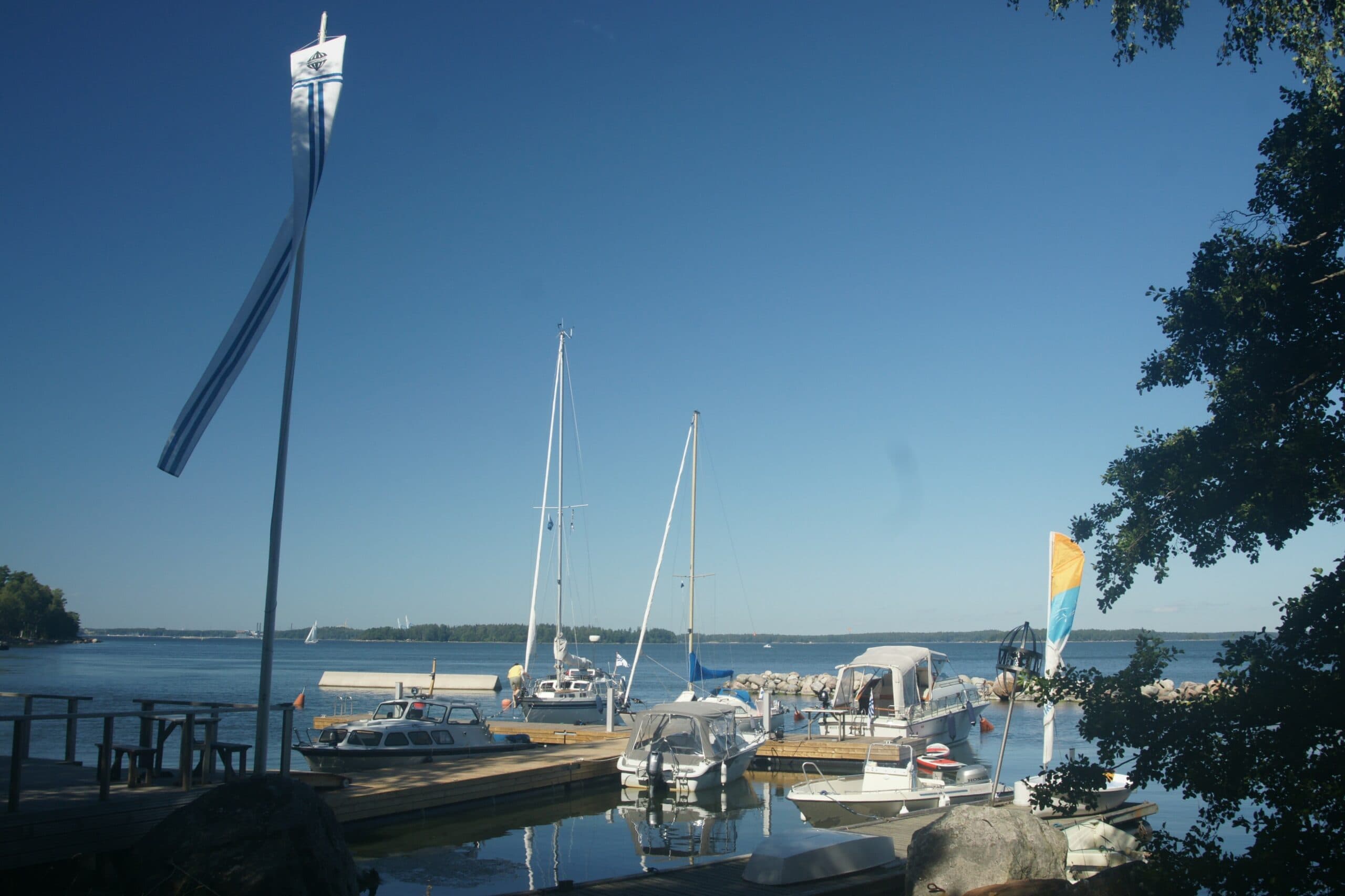 The harbour at Musta Hevonen: wooden jetty, the club pennant flying, boats moored in calm water under bright sun.