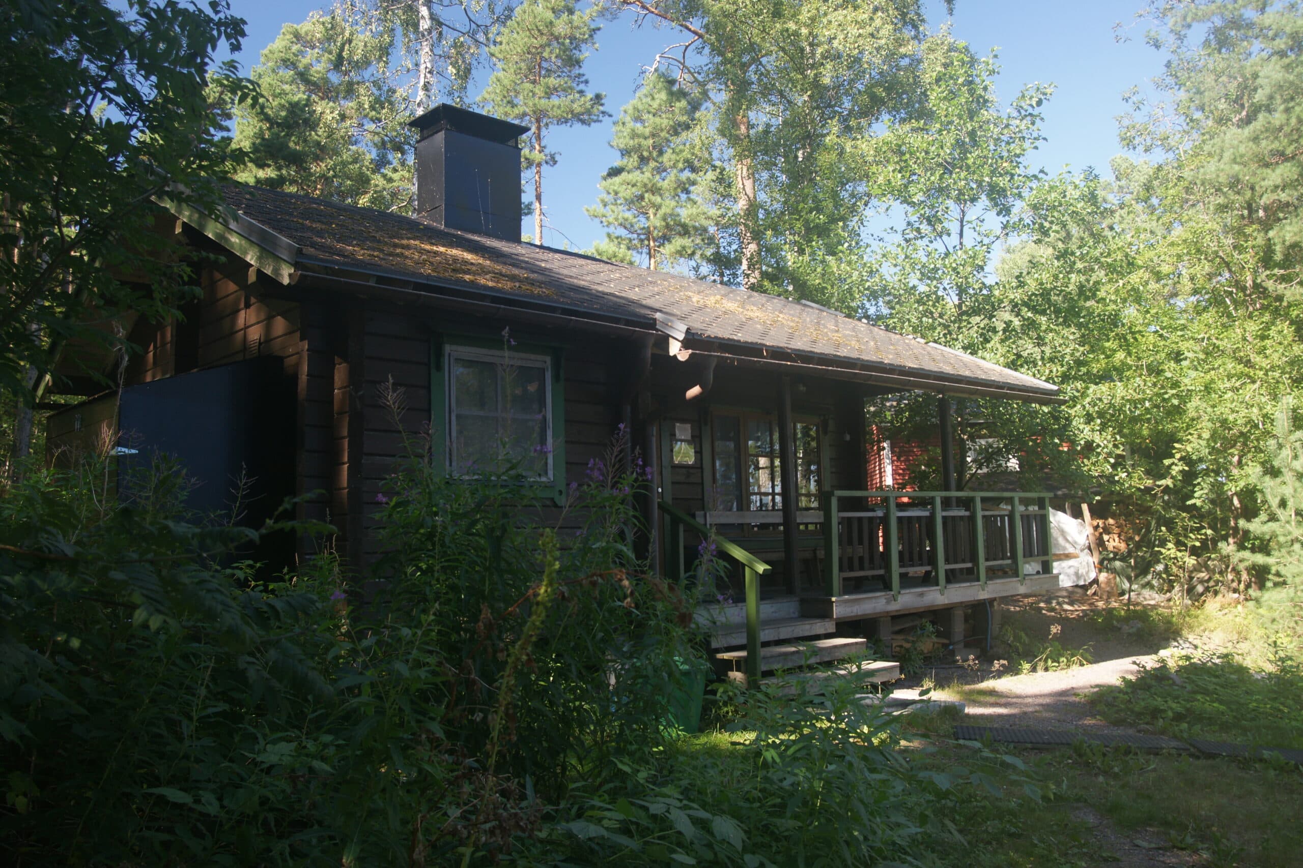 The sauna on Musta Hevonen: a small dark-stained timber building with a tall chimney, set in pine forest.
