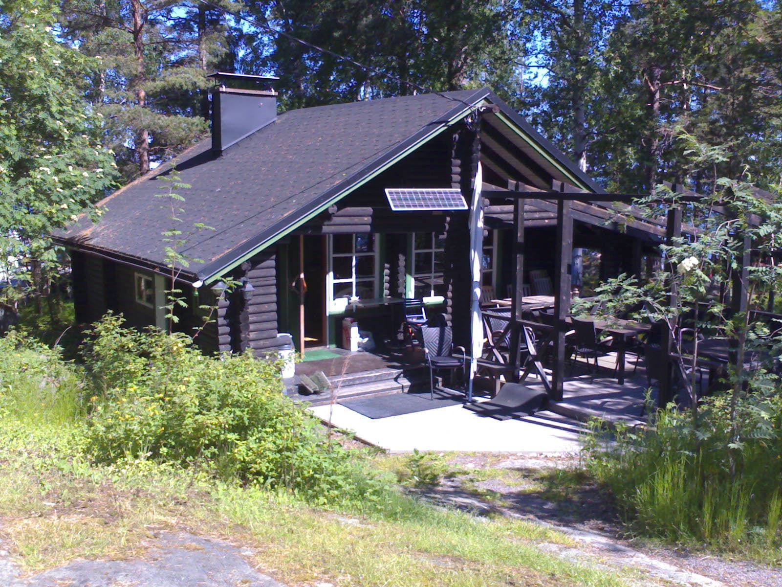 The main building on Musta Hevonen: a dark-stained log house with a deep covered terrace among pines.